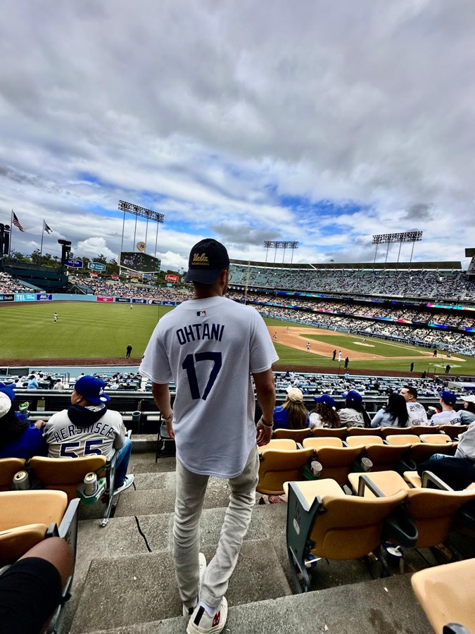A fan in a Dodgers jersey watching a baseball game from the stands
